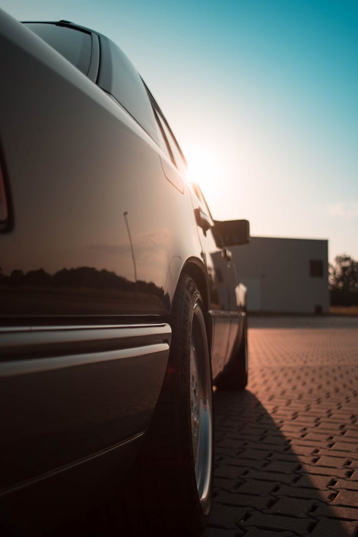 who-we-are A parked sedan reflects sunlight on a paved surface during the day, highlighting automotive design.